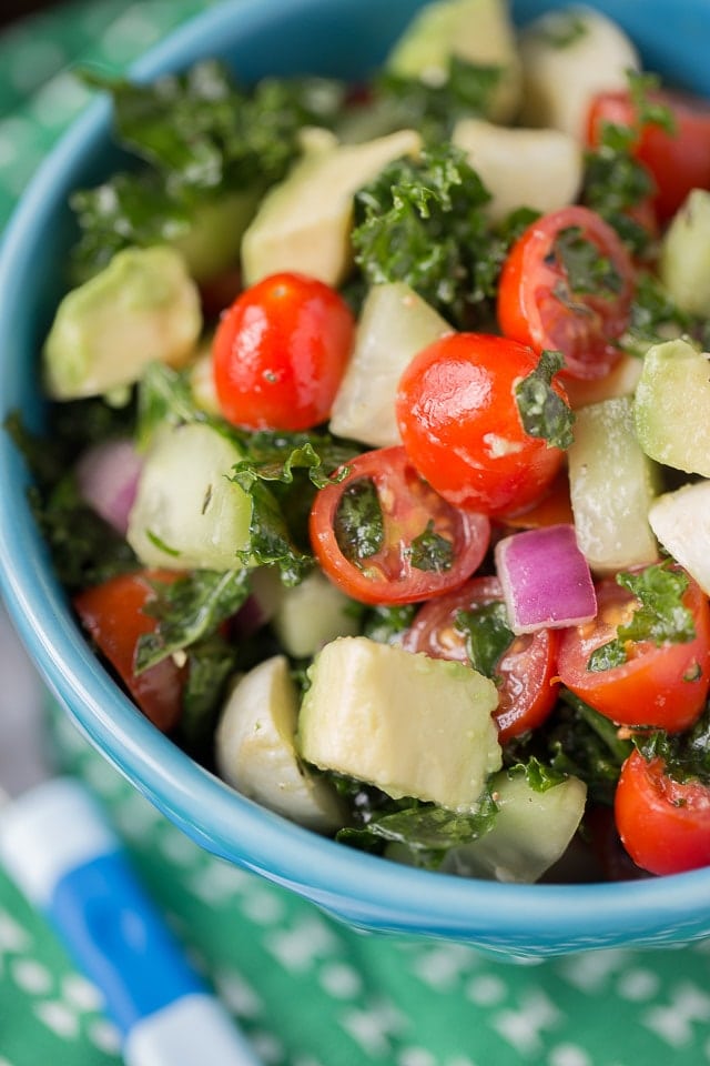 Chopped kale salad with red onion and cherry tomatoes in a blue bowl.