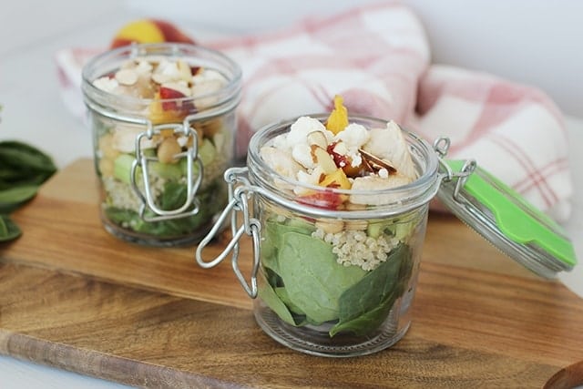 sweet and savory peach quinoa salad in a mason jar on a wooden cutting board.