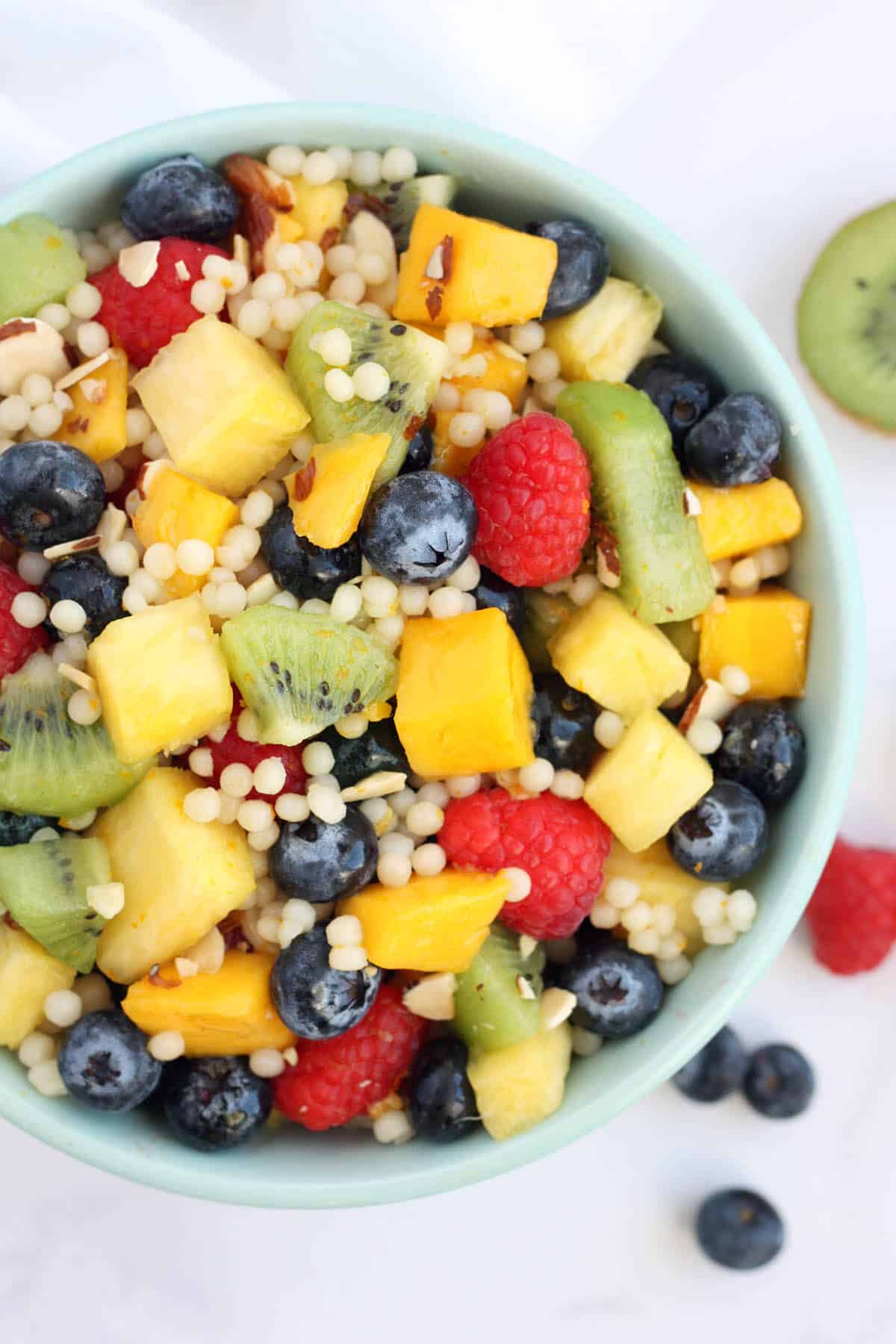 A blue bowl filled with fruit salad with couscous and toasted almonds.